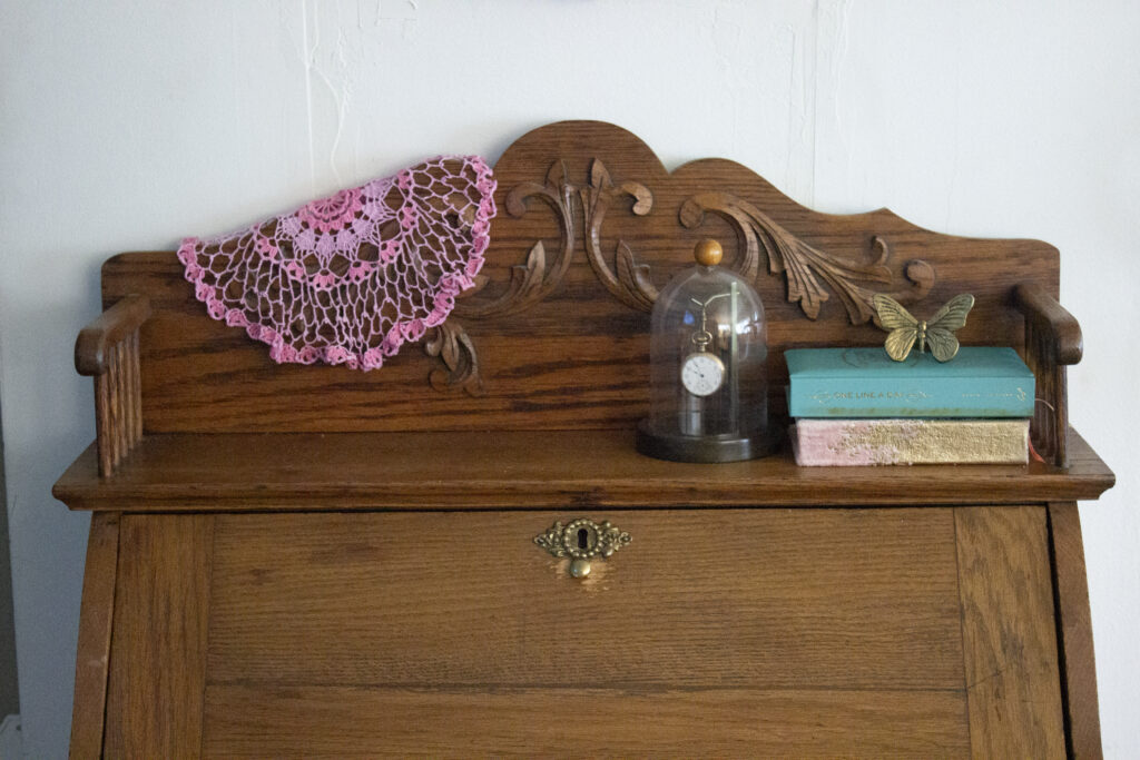 Vintage secretary desk styled with a vintage pocketwatch, books, a butterfly, and a pink doily