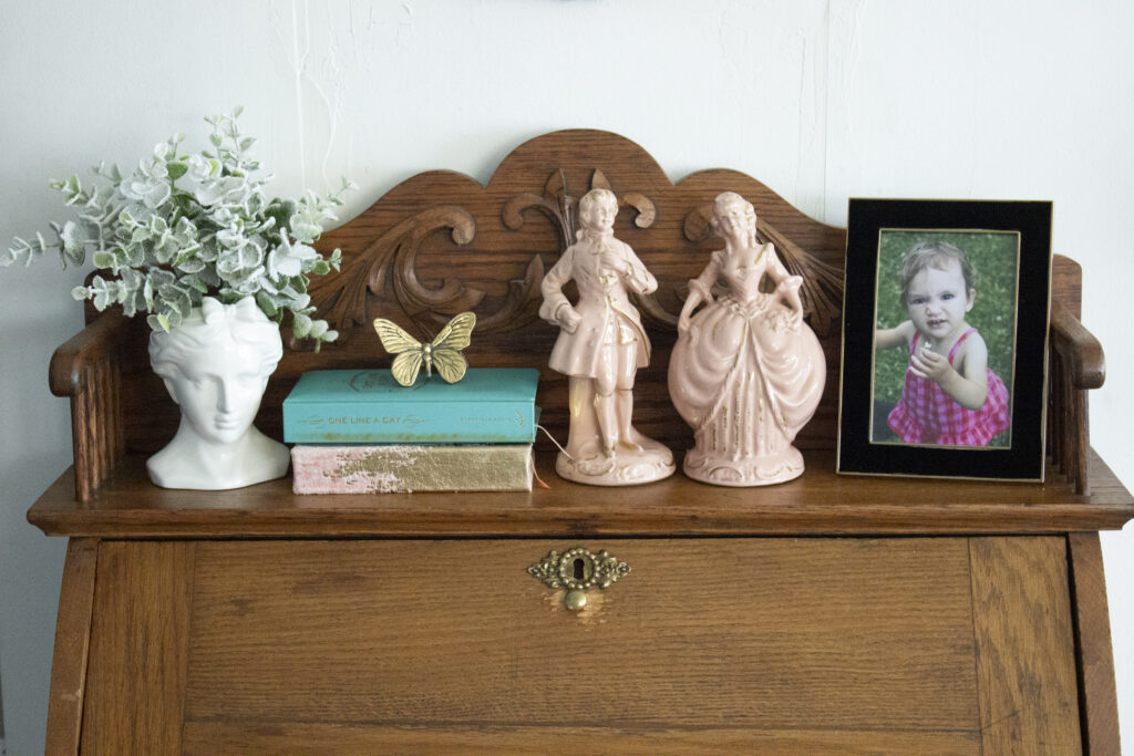 Vintage secretary desk styled with a bust, French figurines, books, a butterfly, and a picture frame