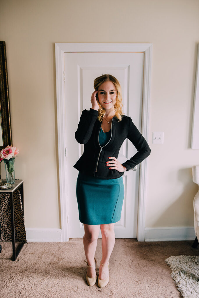 Woman in fitted green sheath dress and black peplum blazer