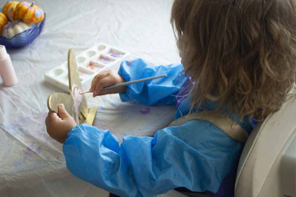 Little girl painting wooden butterfly